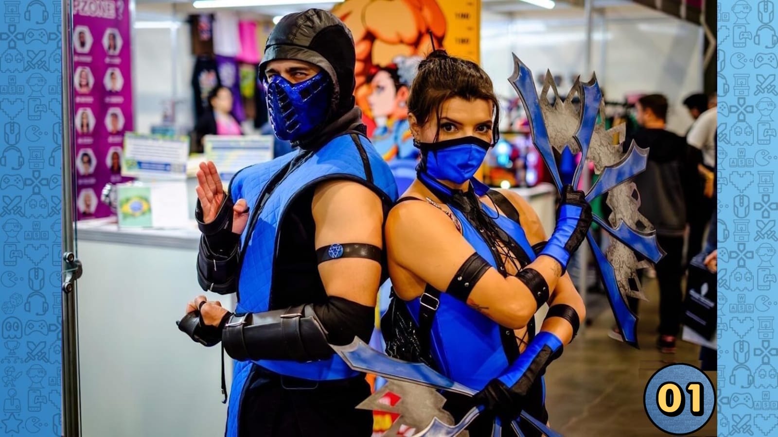 Duas pessoas em cosplay de Sub‑Zero e Kitana, usando trajes azul e preto com máscaras. Kitana segura leques decorados. Estão de costas um para o outro em ambiente de convenção.