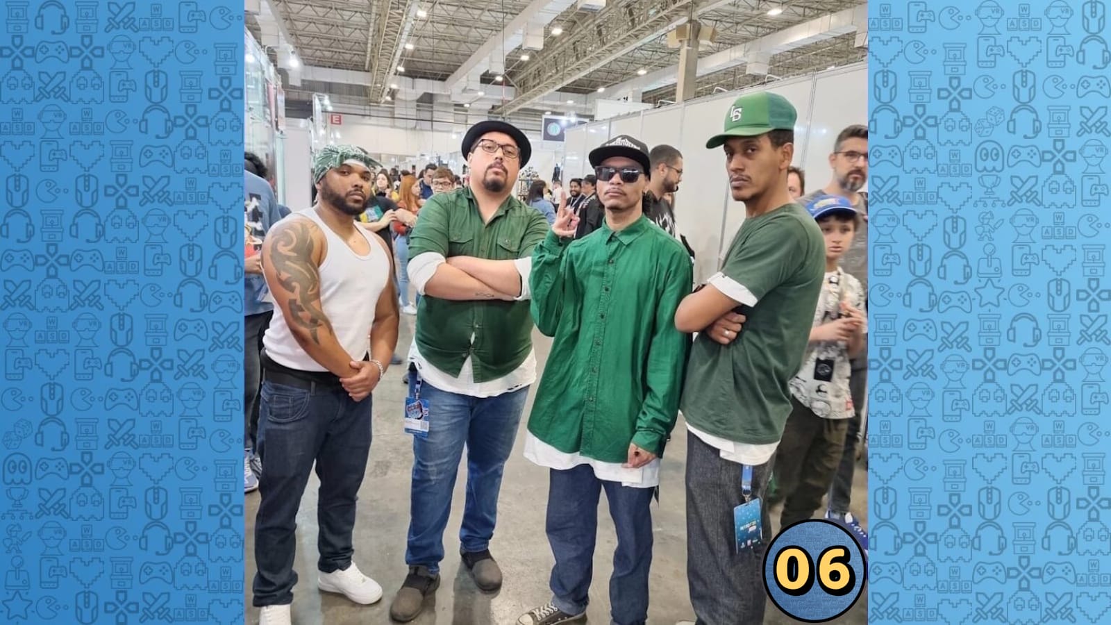 Quatro pessoas posam juntas em evento com estandes ao fundo. Três usam camisetas verdes e uma usa regata branca. 