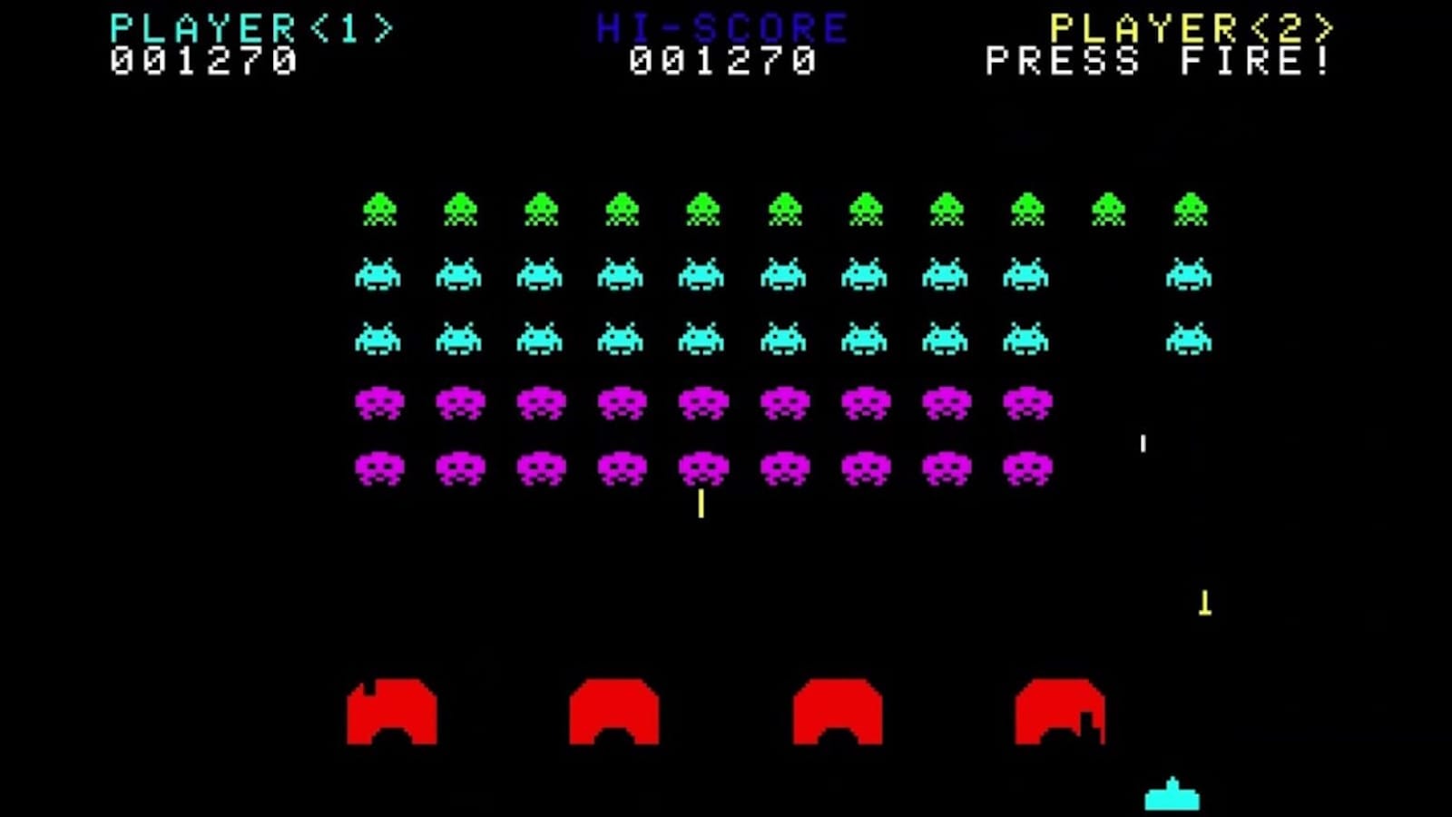 Tela de Space Invaders com fileiras de alienígenas verdes, azuis e roxos, nave azul na base e escudos vermelhos, pontuação no topo.