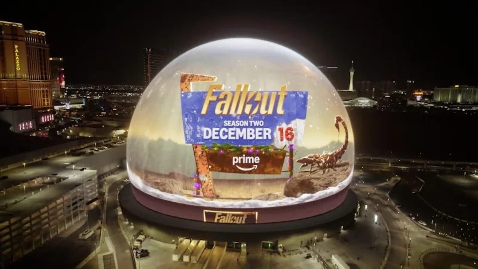 Estrutura esférica iluminada à noite exibindo cena digital com escorpião gigante no deserto e placa com texto ‘Fallout Season Two December 16 Prime’.