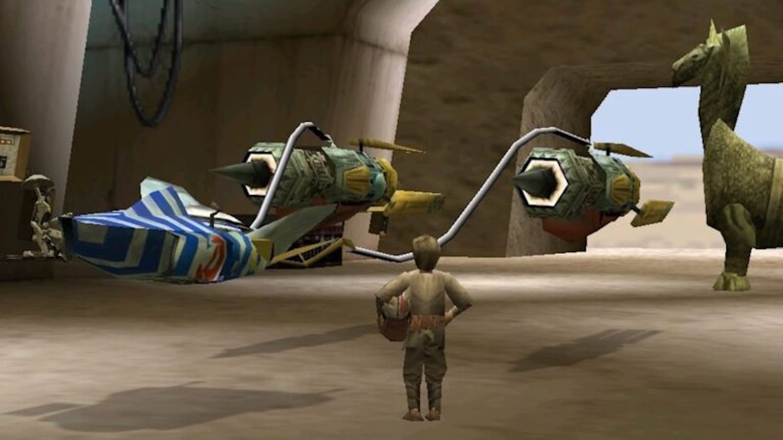 Cena de jogo em ambiente desértico com um personagem visto de costas diante de um podracer composto por dois motores grandes ligados a uma cabine pequena azul e branca. O chão é arenoso e as paredes são de pedra.